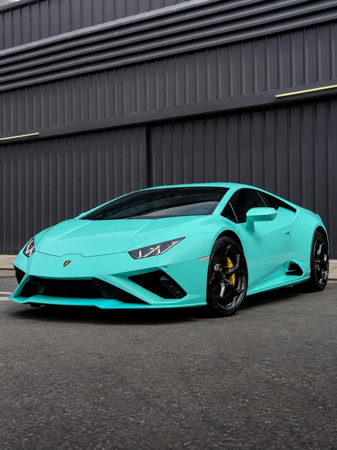 Huracan EVO RWD: Lamborghini Huracan EVO RWD 2024 in Electric Aqua, front three-quarter view parked in front of a dark industrial building