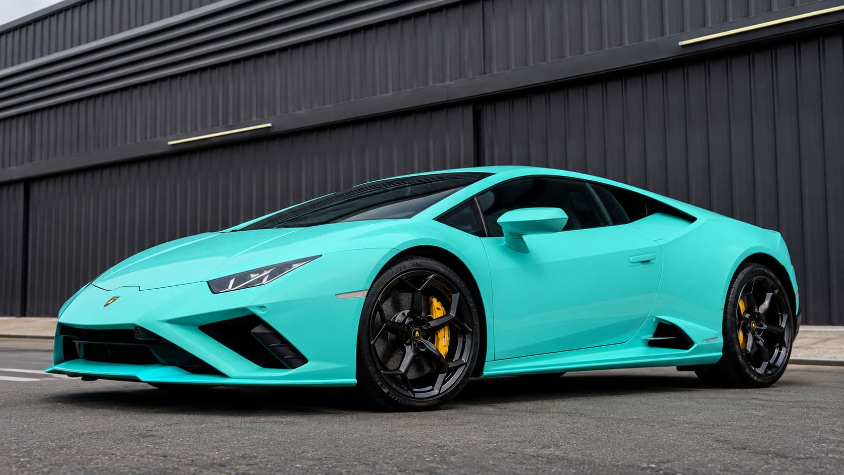 Huracan EVO RWD: Lamborghini Huracan EVO RWD 2024 in Electric Aqua, low front three-quarter view beside a dark industrial building