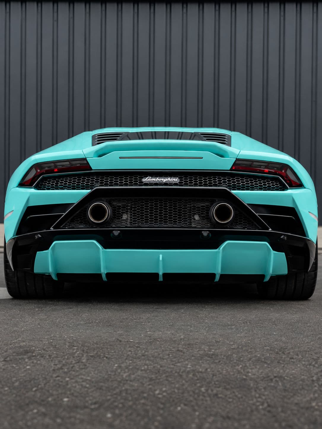 Huracan EVO RWD: Lamborghini Huracan EVO RWD 2024 in Electric Aqua, low rear view in front of a dark industrial building