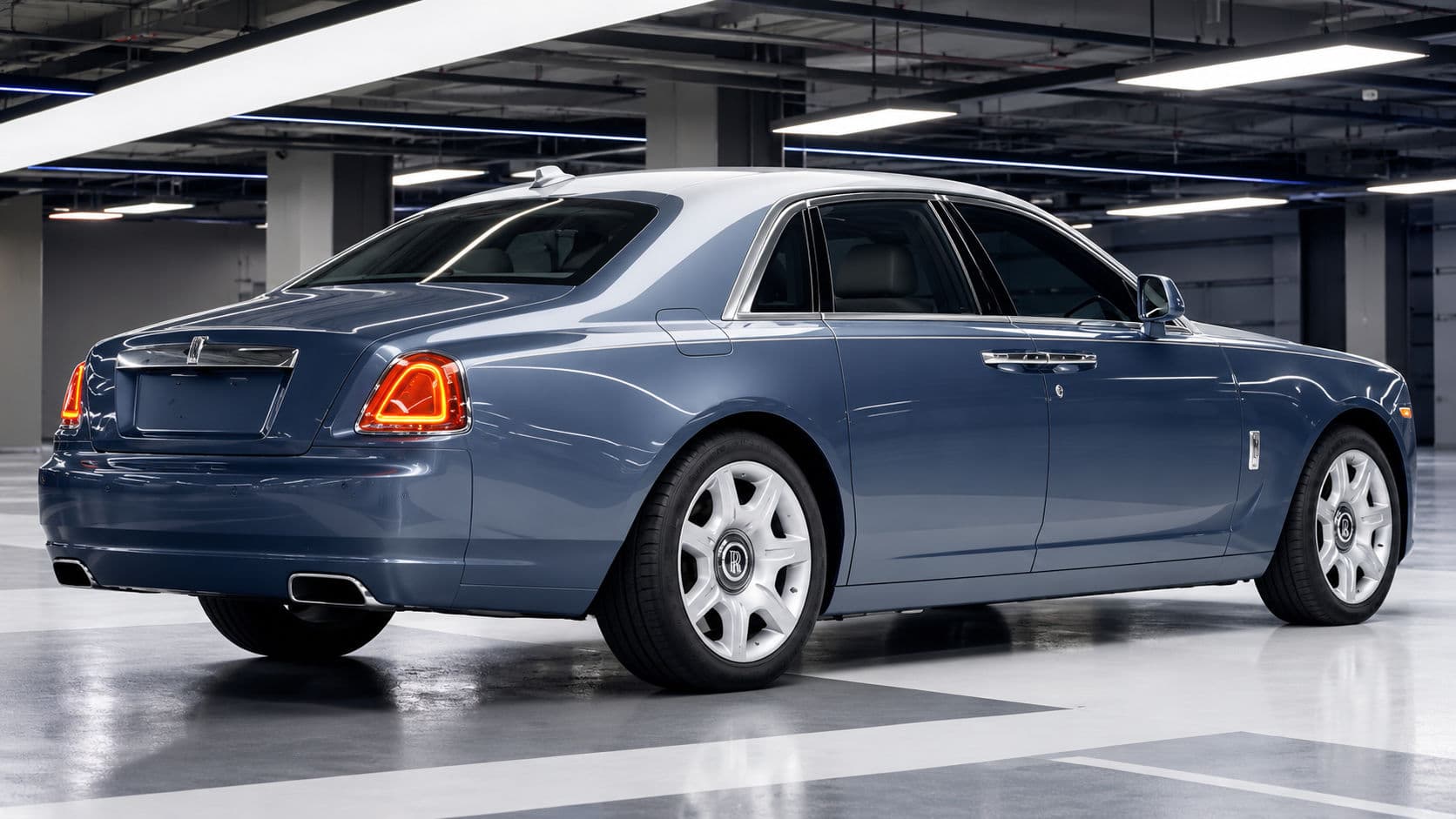 Ghost: Rolls-Royce Ghost 2019, rear three-quarter view in an indoor garage, steel blue body with silver bonnet and roof, illuminated LED taillights and chrome exhaust finishers