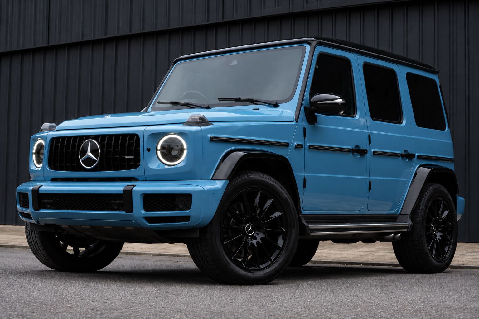 G350: Mercedes-Benz G350 2022 in Vintage Blue, front three-quarter view with illuminated headlights against a dark industrial wall
