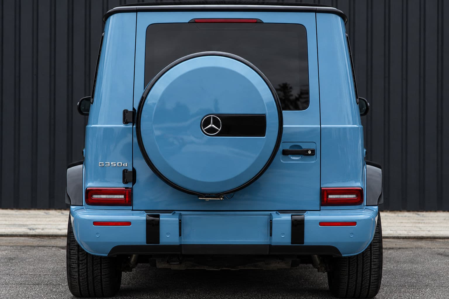 G350: Mercedes-Benz G350 2022 in Vintage Blue, rear view with spare wheel cover against a dark wall