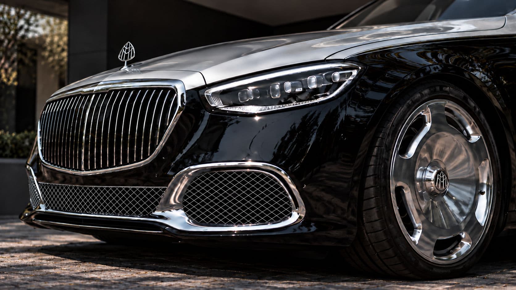 S 680: Mercedes-Maybach S 680 2025 front detail with the chrome Maybach grille, hood ornament, headlight and polished monoblock wheel