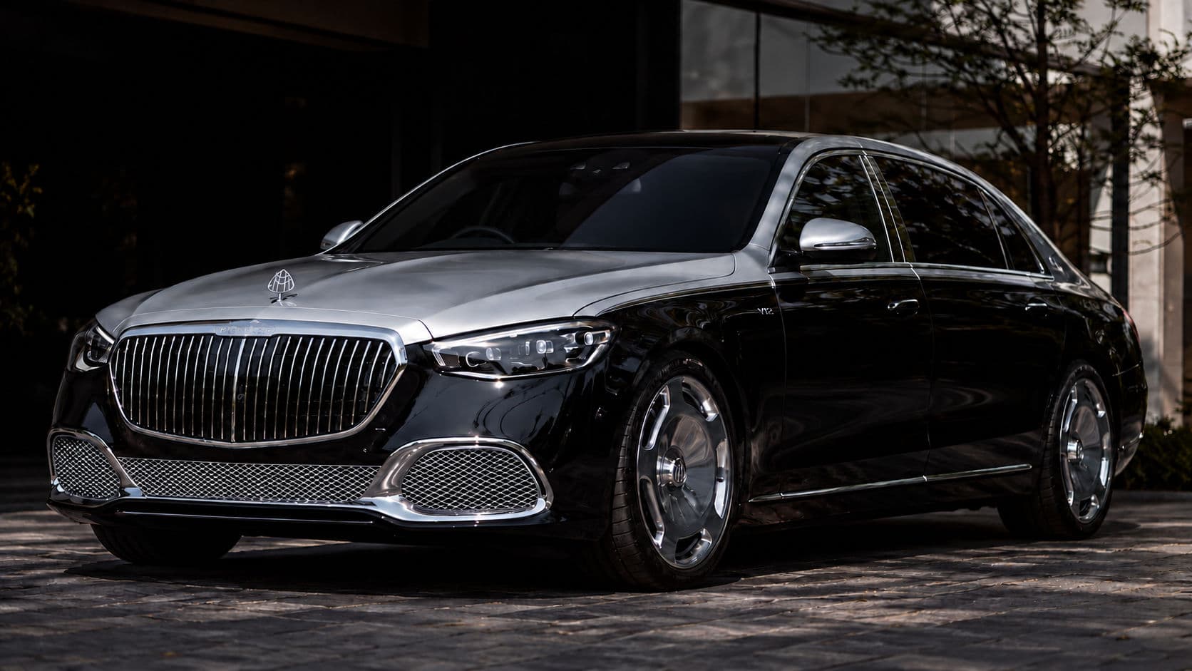S 680: Mercedes-Maybach S 680 2025 in two-tone silver and black, front three-quarter view on a paved courtyard in front of a dark building