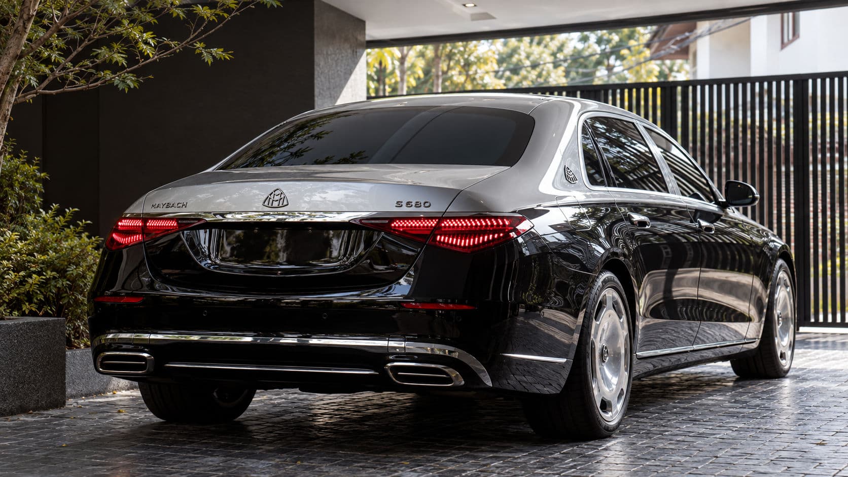 S 680: Mercedes-Maybach S 680 2025 in two-tone silver and black, rear three-quarter view under a carport by a black slatted gate