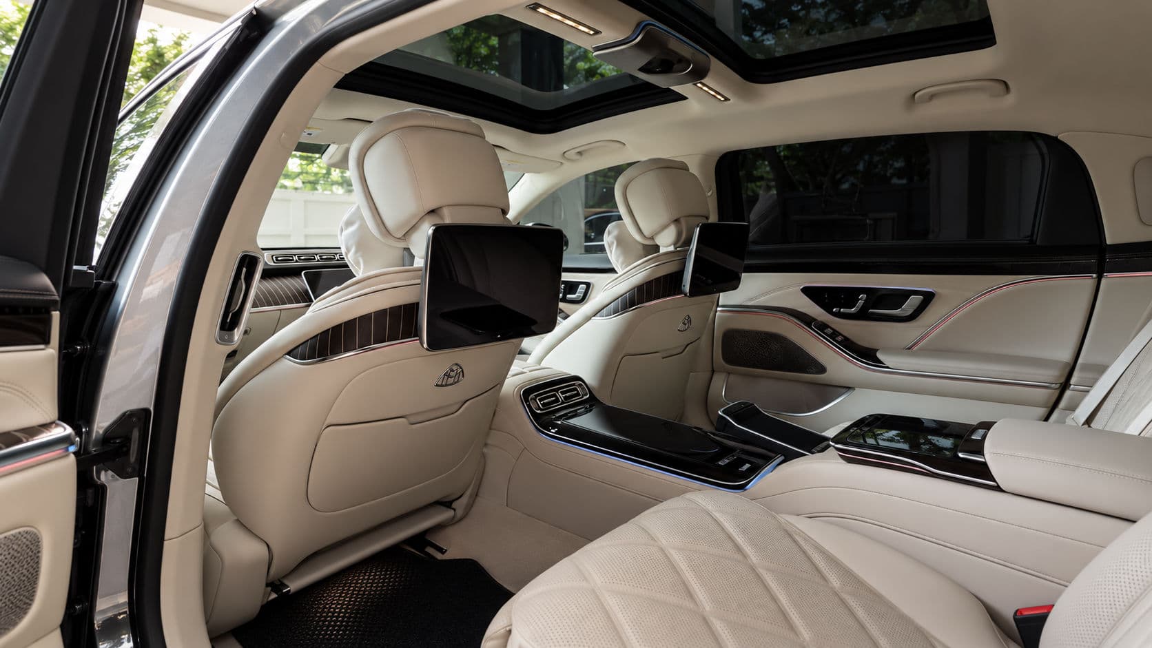 S 680: Mercedes-Maybach S 680 2025 rear cabin in cream leather with diamond-quilted seats, seatback screens and a panoramic sunroof, seen through the open rear door